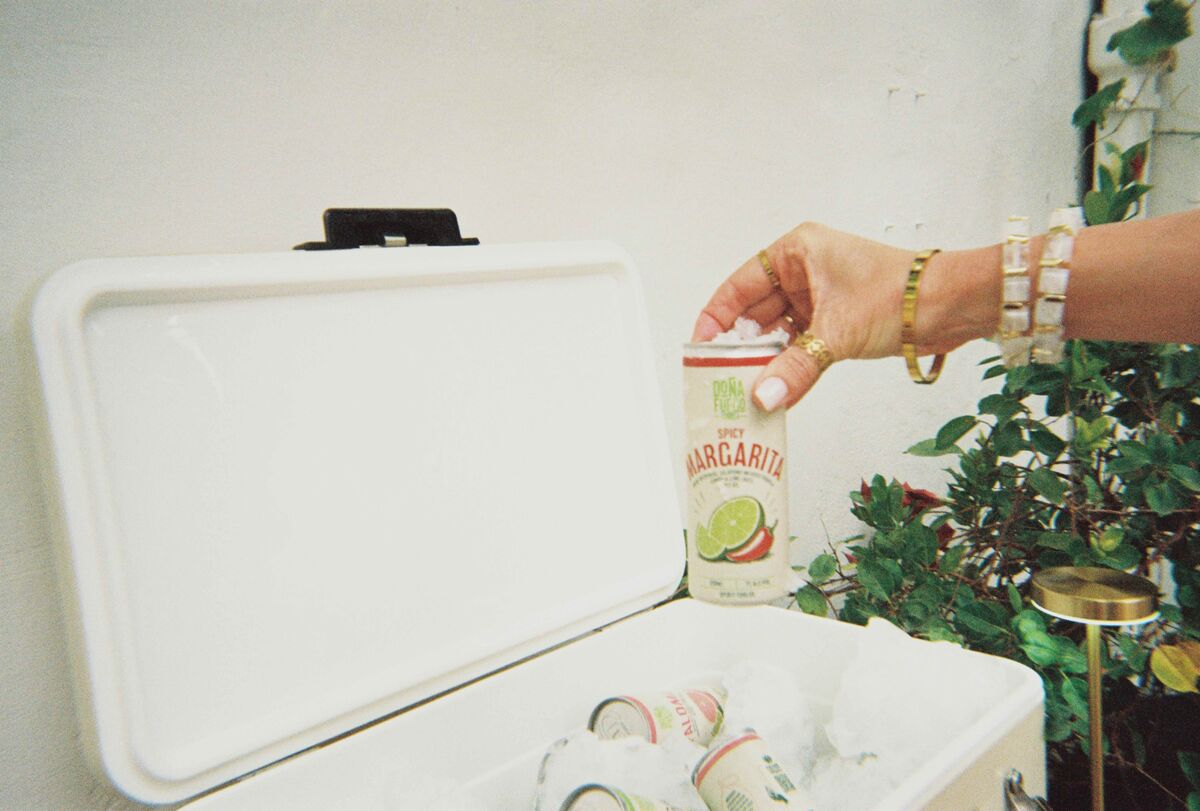 A hand lifting a Spicy Margarita can out of a white cooler box