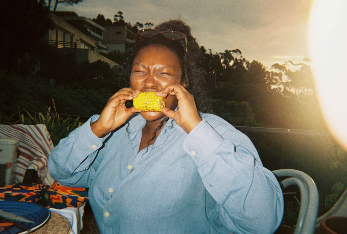 A guest biting into corn on the cob at sunset, with a light leak across the frame