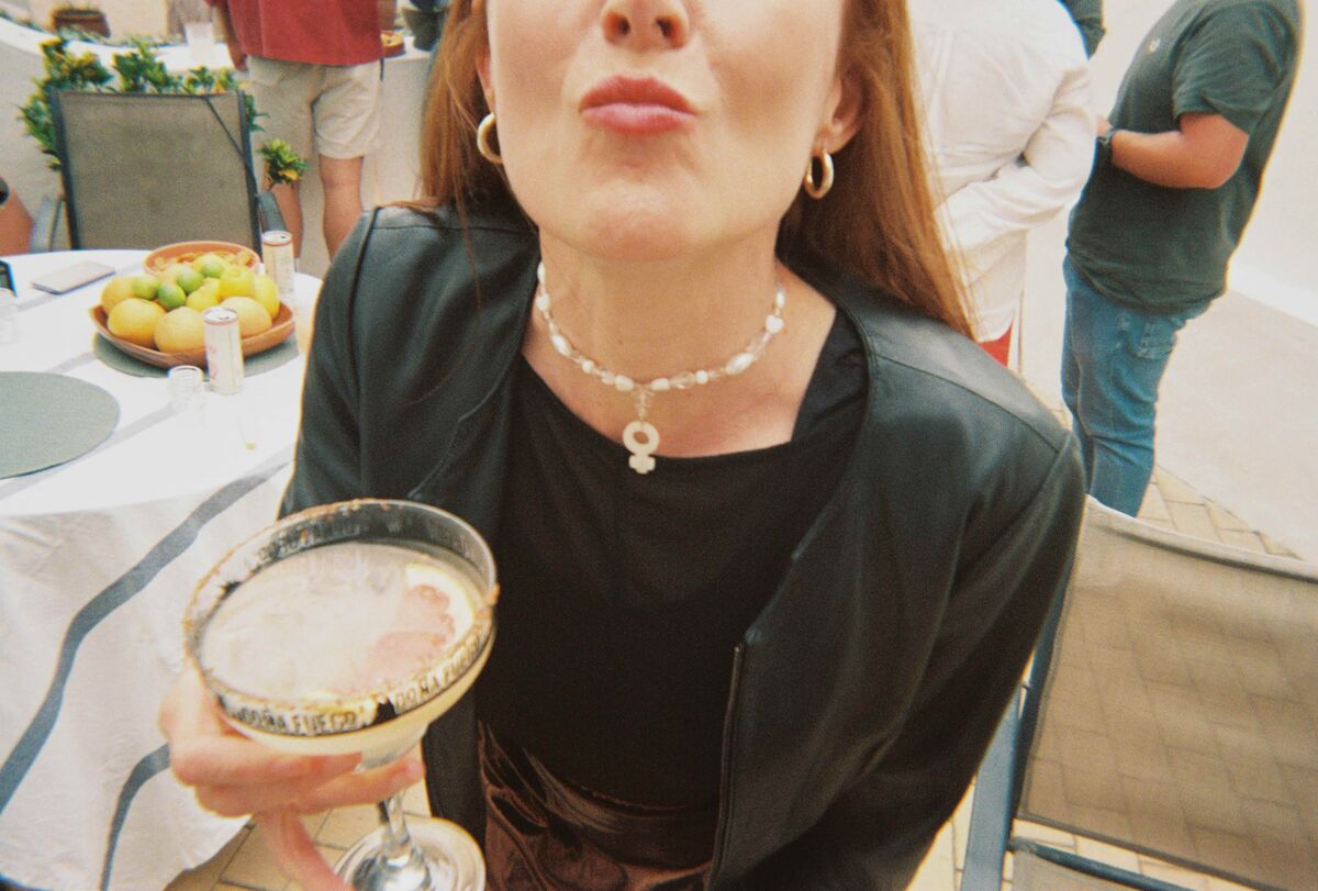 A guest blowing a kiss to the camera, holding a Doña Fuego cocktail in a coupe glass