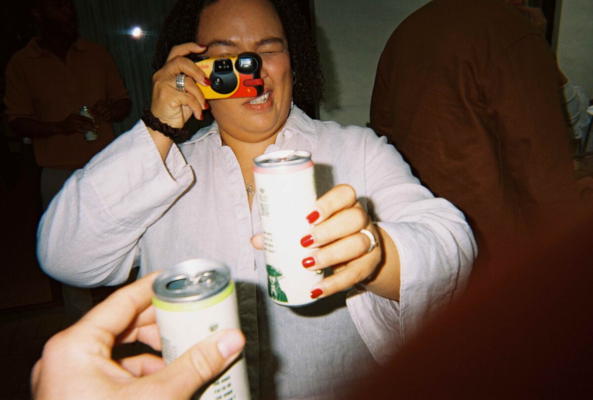 A guest holding up a disposable camera and a Paloma can, cheersing towards the lens