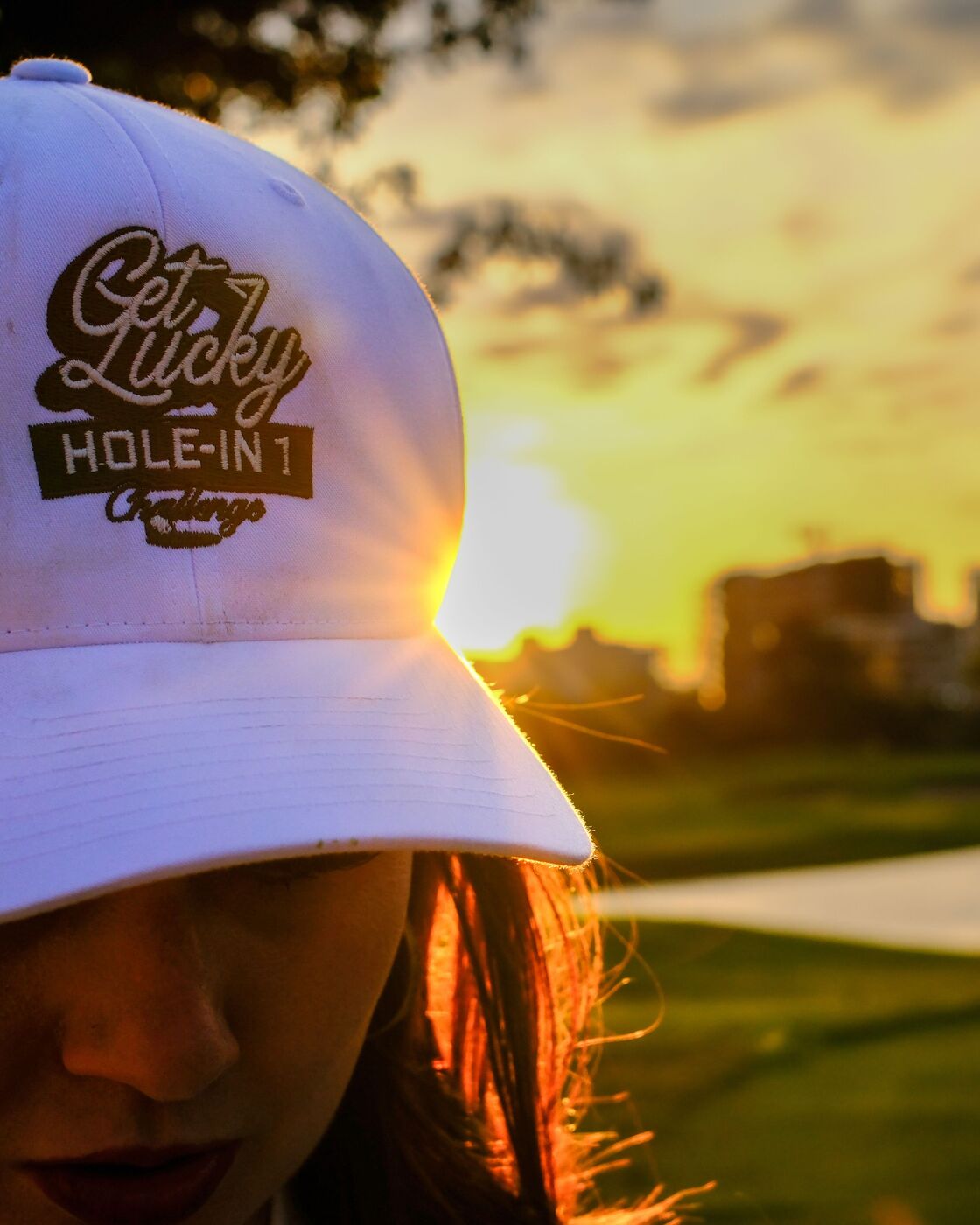 A golfer in a Get Lucky Hole-in-1 Challenge cap, backlit by the sunset on the course